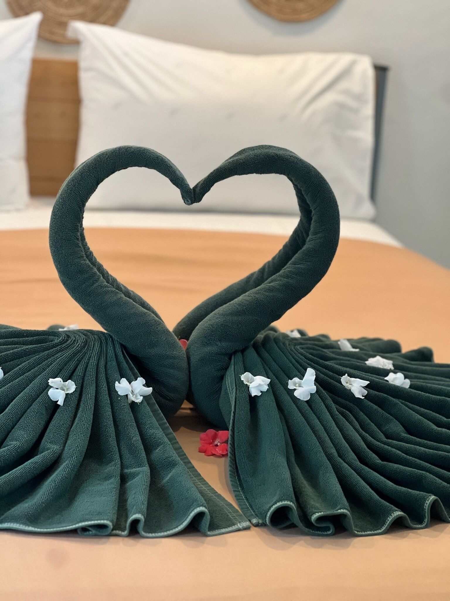 Una cama con una toalla dispuesta en forma de corazón y flores blancas.