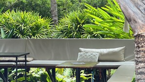 A covered outdoor seating area with a bench and table, surrounded by lush greenery and a palm tree. - The Canopy Krabi (Krabi)