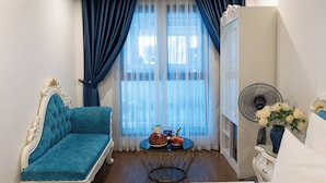 A room with a blue sofa, a round table with fruits and drinks, a fan, and a cabinet with flowers. - Royal Hotel Thanh Tri (Hanoi)