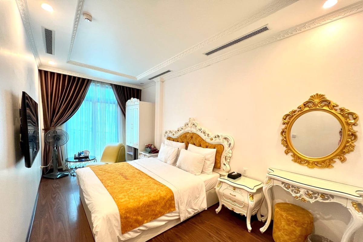 A hotel room with a large bed, a bedside table, a mirror, and a chair.