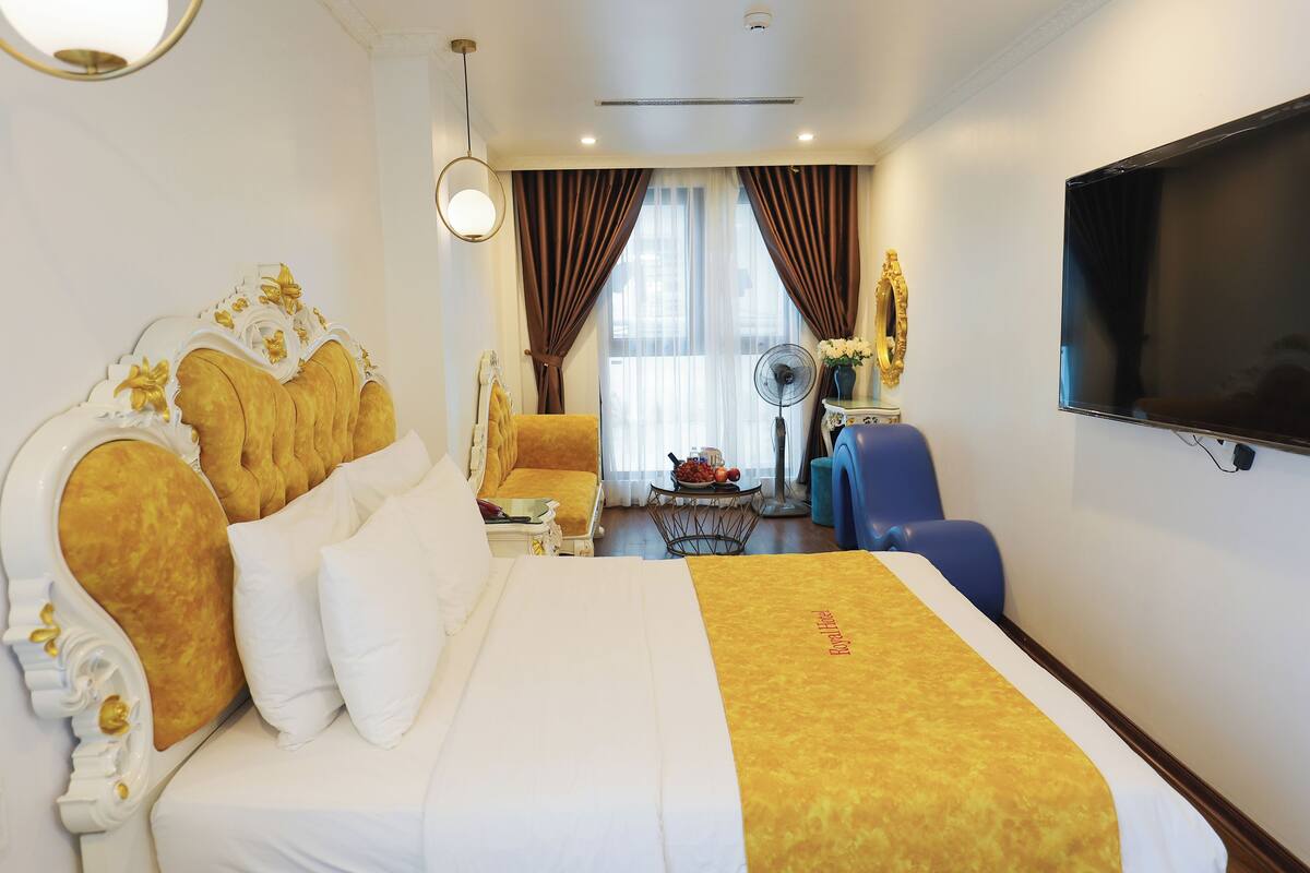 A hotel room with a large bed, a flat-screen TV, a desk with a fan, and a view of the outdoors through the window.