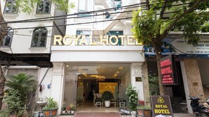 The exterior of the Royal Hotel with a prominent entrance, potted plants, and a sign indicating the hotel's name and distance from the entrance. - Royal Hotel Thanh Tri (Hanoi)
