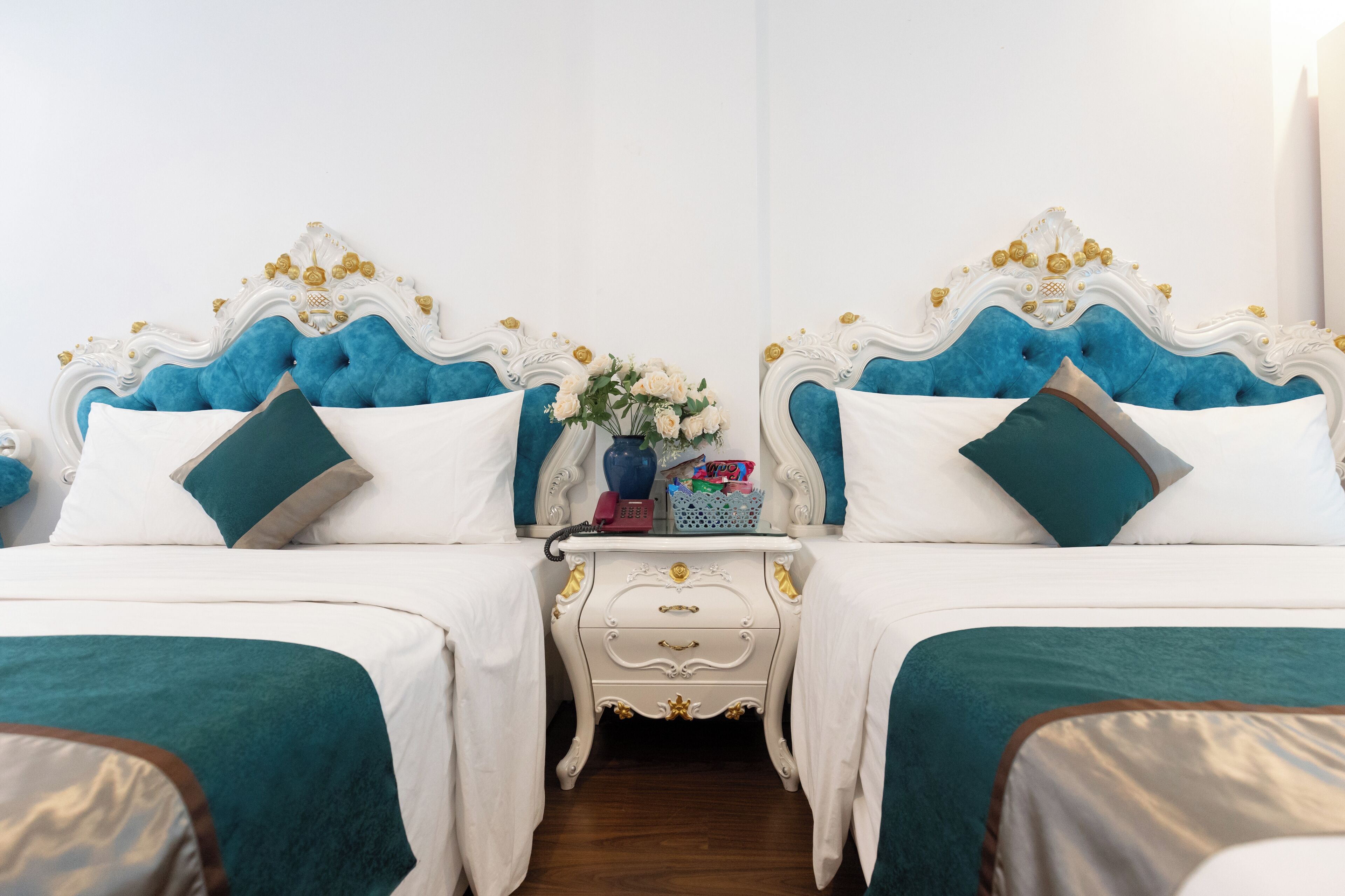Una cama doble con cabecera blanca y azul, una mesita de noche con un florero y un reloj pequeño.