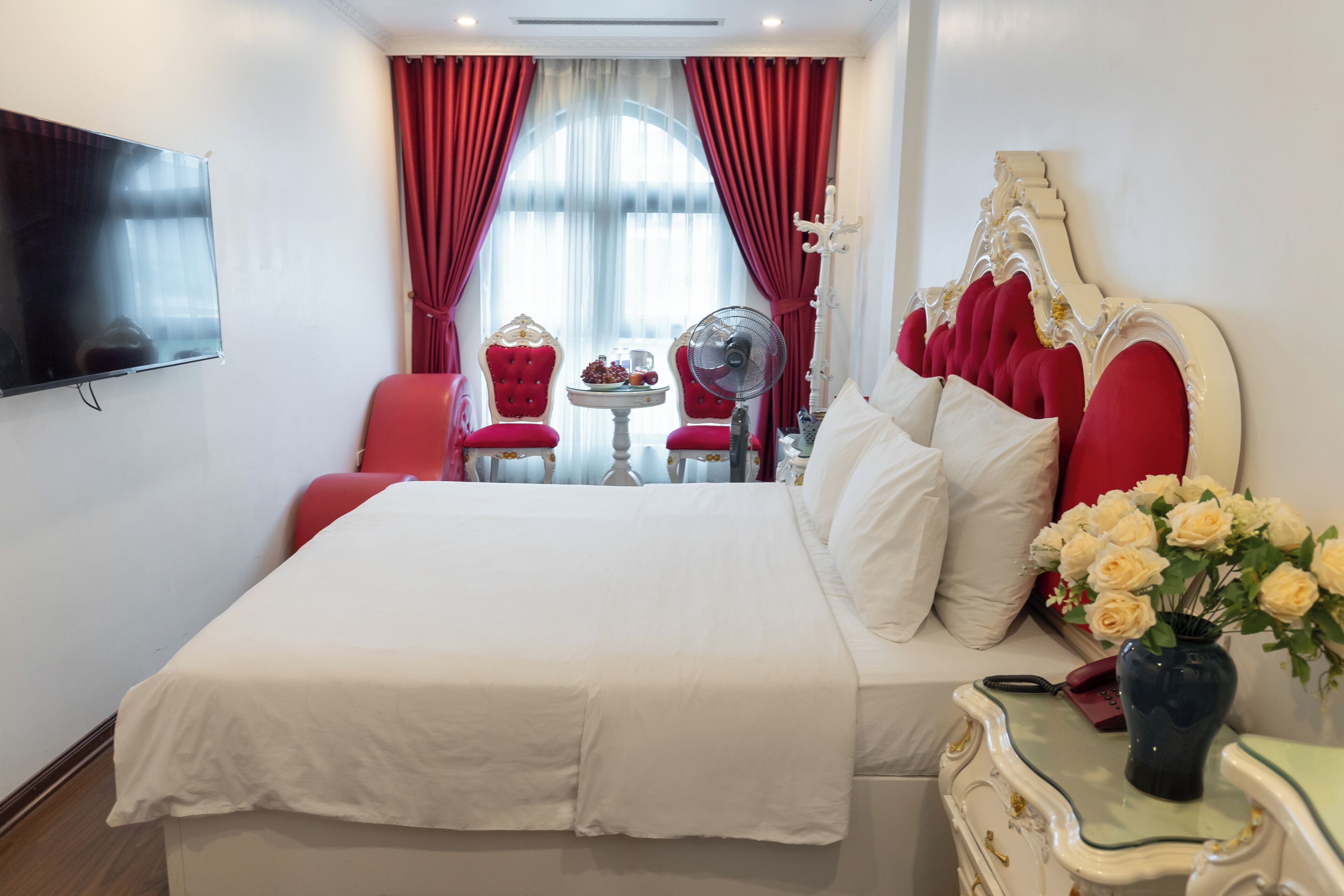 Een hotelkamer met een groot bed, een televisie, een tafel met stoelen en een bloevas.