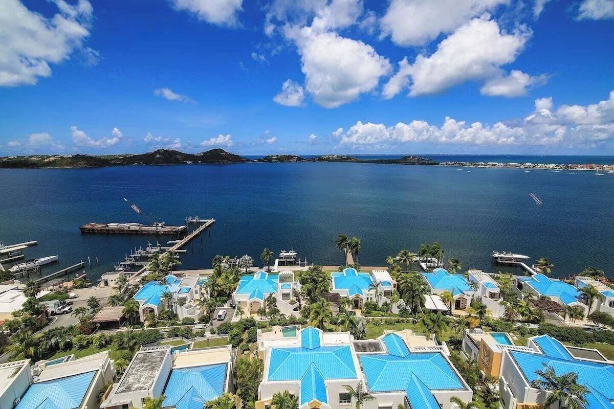 Ein Küstenort mit mehreren Gebäuden, die blaue Dächer haben, einer Marina und freiem Blick auf das Meer und entfernte Inseln.