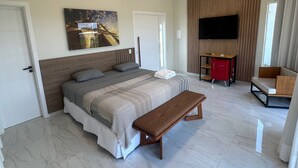 Une chambre moderne avec un grand lit, un banc, une télévision et un bureau.