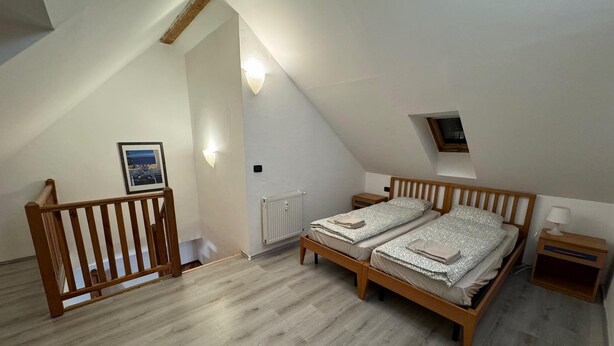 Une chambre avec deux lits, une tête de lit en bois, une table de chevet, un tableau encadré et un radiateur.