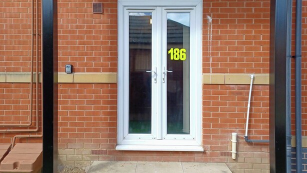 A brick building with a white-framed double door, a number '186' on the glass, and a small step leading to the entrance.