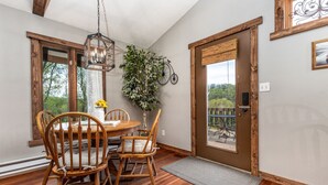A dining area with a wooden table and chairs, a hanging light fixture, and a view through the door.