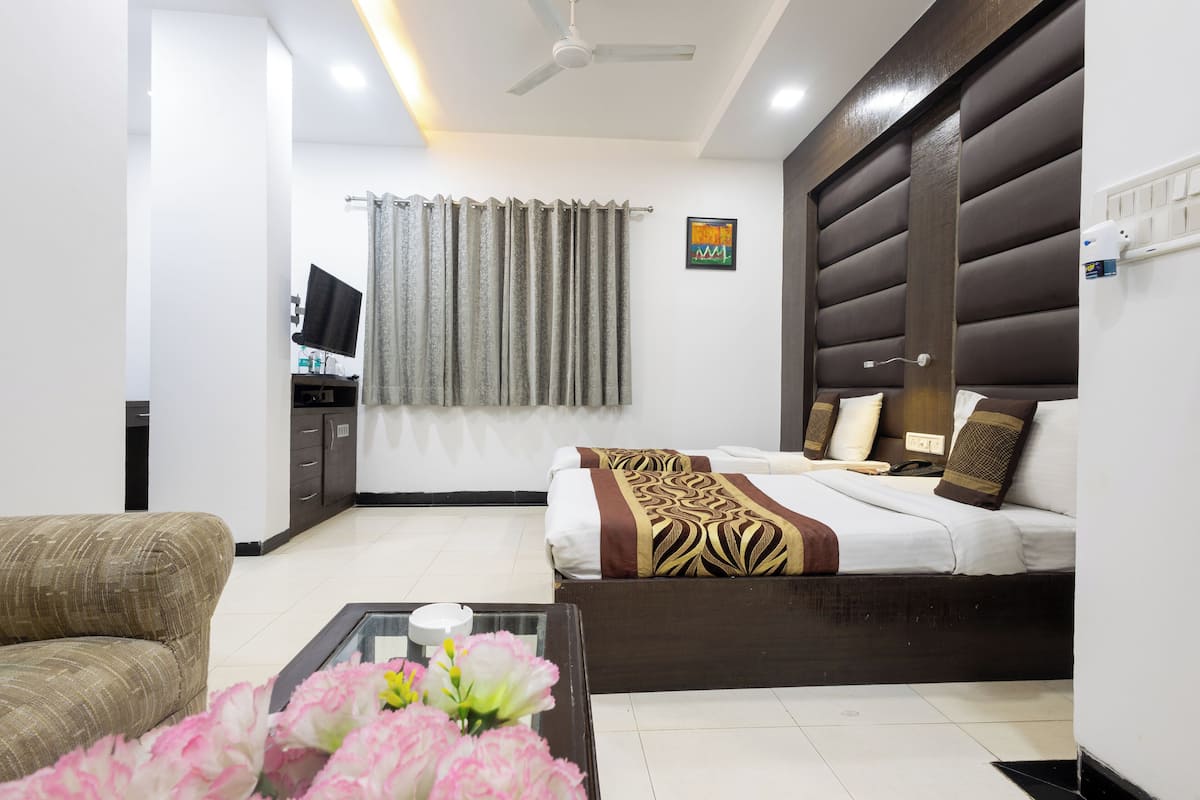 A hotel room with a bed, a sofa, a TV, a desk, and a window with curtains.