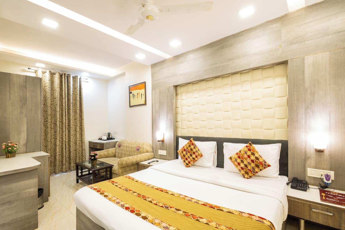 A hotel room with a large bed, a desk, a sofa, and a shower area.