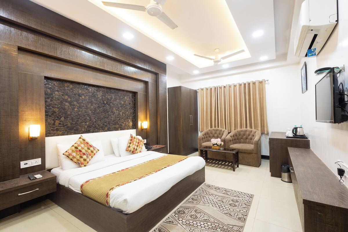 A modern hotel room with a large bed, a desk, a chair, a TV, and a ceiling fan.