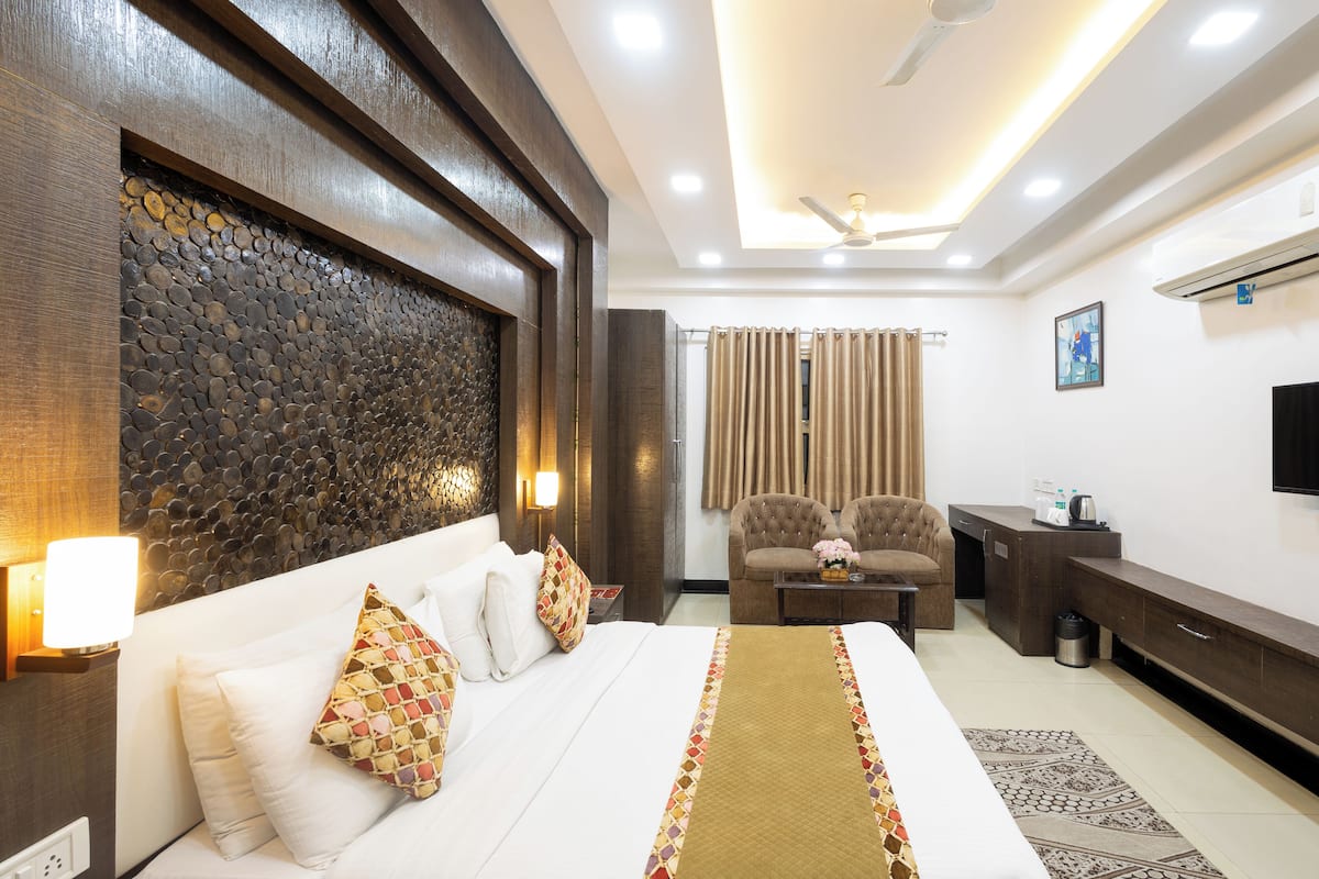 A hotel room with a large bed, a sofa, a TV, and a ceiling fan.