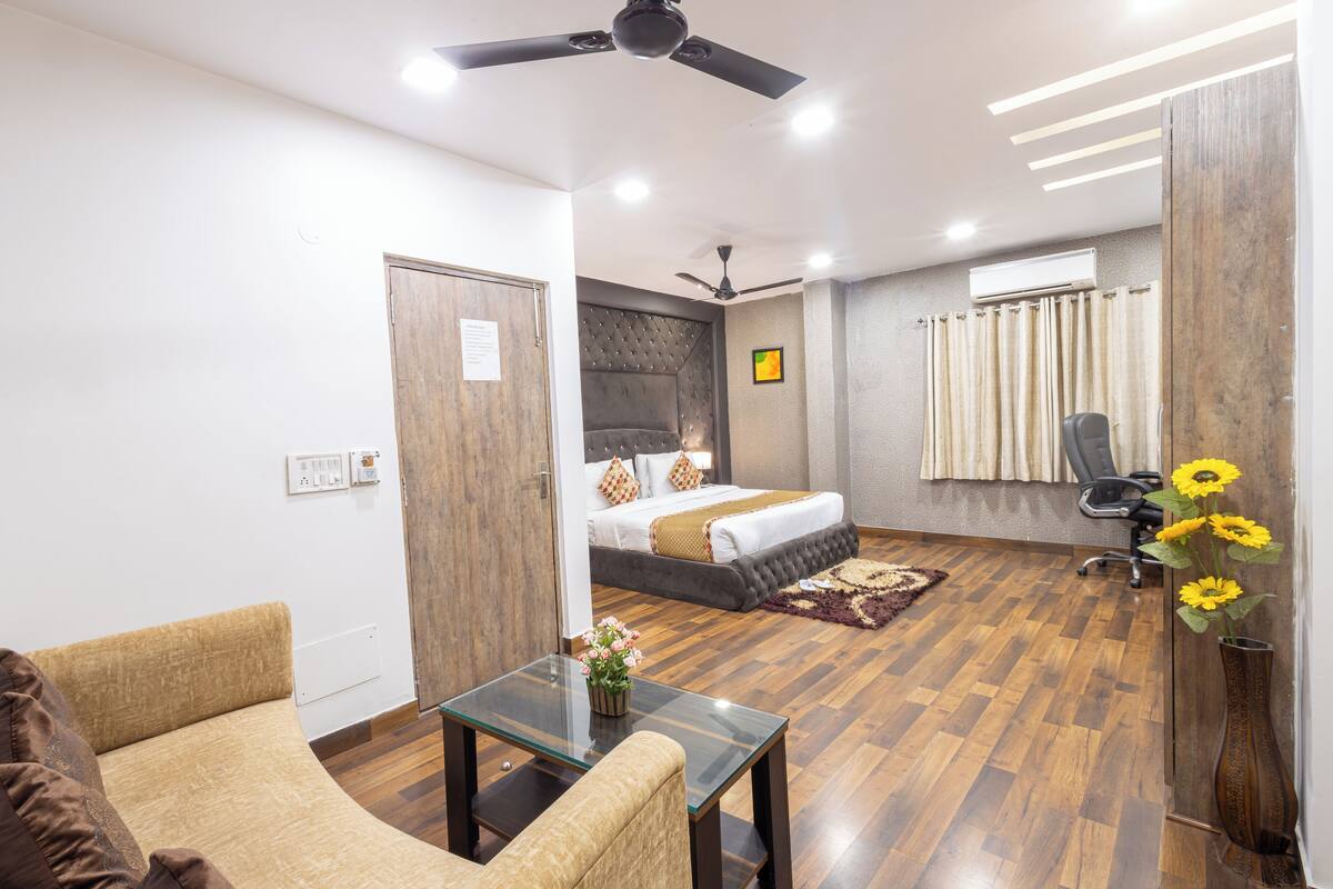 A modern hotel room with a bed, a glass table with flowers, a sofa, and a ceiling fan.