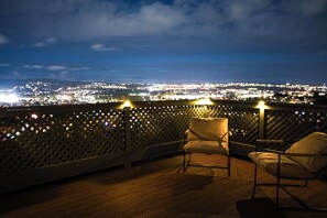 Un balcon avec deux chaises et une vue sur le paysage urbain illuminé la nuit.