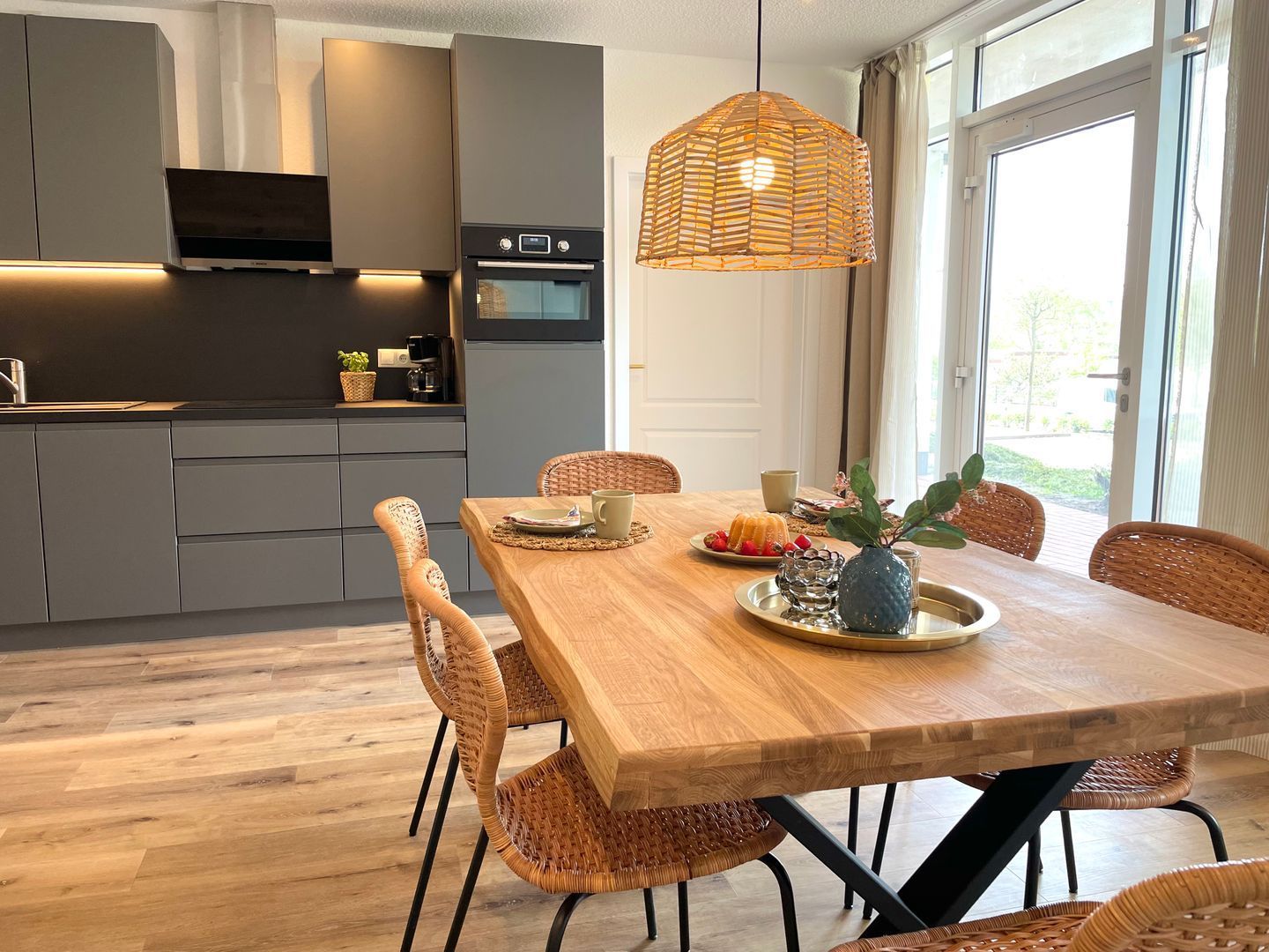 Eine moderne Küche mit grauen Schränken, einem eingebauten Ofen und einem Essbereich mit Holztisch und Korbstühlen.