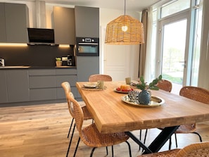 Eine moderne Küche mit grauen Schränken, einem eingebauten Ofen und einem Essbereich mit Holztisch und Korbstühlen.