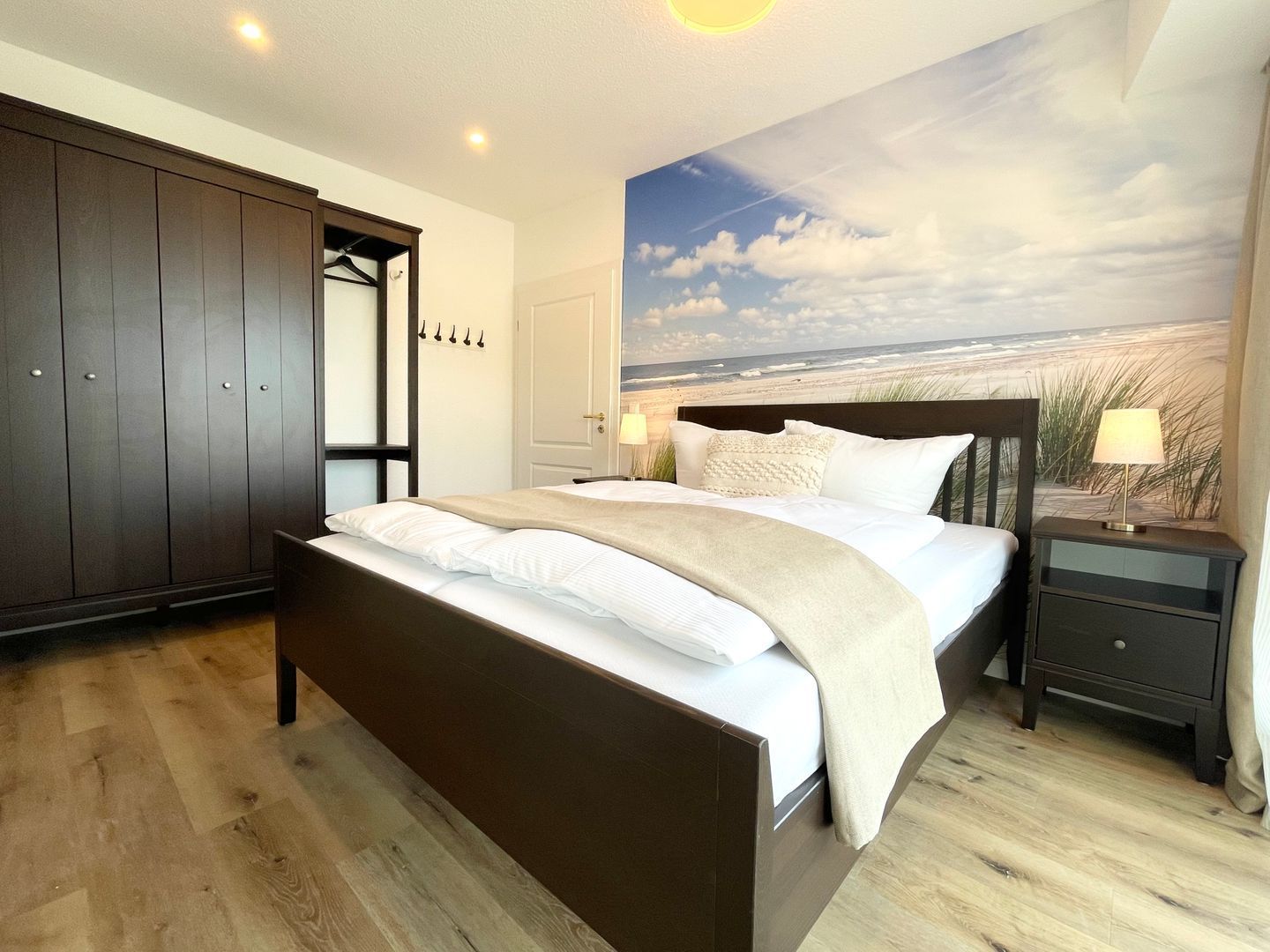 Ein Schlafzimmer mit Bett, Kleiderschrank, Nachttisch und Wandbild mit Strandmotiv.