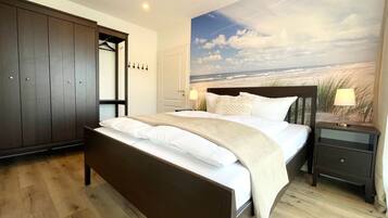 Ein Schlafzimmer mit Bett, Kleiderschrank, Nachttisch und Wandbild mit Strandmotiv.
