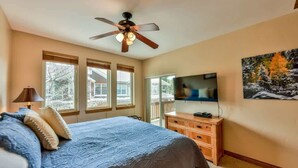 A bedroom with a bed, a ceiling fan, a TV, and a painting on the wall.