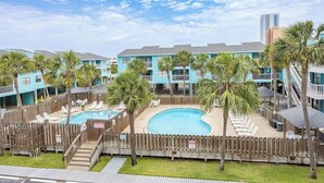 Een resort met meerdere blauwe gebouwen, een centraal zwembad en palmbomen.