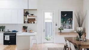 Een moderne keuken met witte kasten, een centraal eiland en een eethoek met een houten tafel en stoelen.