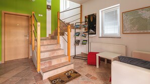 A staircase with a wooden handrail, a red ottoman, a white table, and a map on the wall. - Lavrič Garden Apartment 2 at Lake Bloke, Bloke, Slovenia (Bloke)