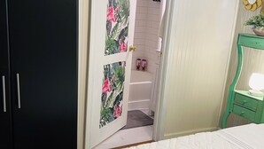 A bedroom with a bed, a wardrobe, a shower area, and a vanity with a mirror.