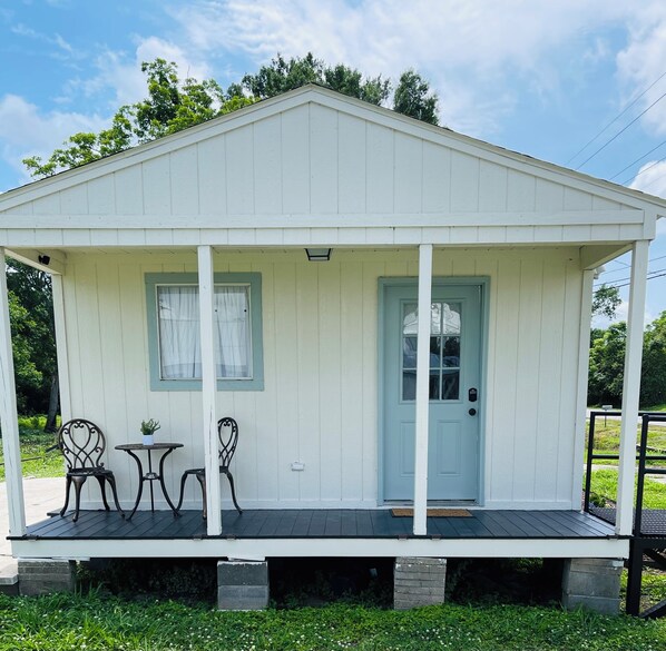 A small, single-story building with a porch, two chairs, and a small table.