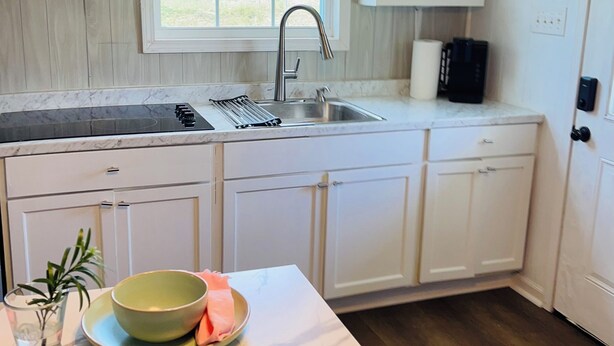 A kitchen with white cabinets, a marble countertop, a sink, and a window with a view of greenery.