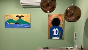 A reception desk with a light wood finish, two wall-mounted air conditioning units, and two paintings depicting abstract figures and landscapes. - B&B CADIFRA PORTAPICCOLA (Naples)