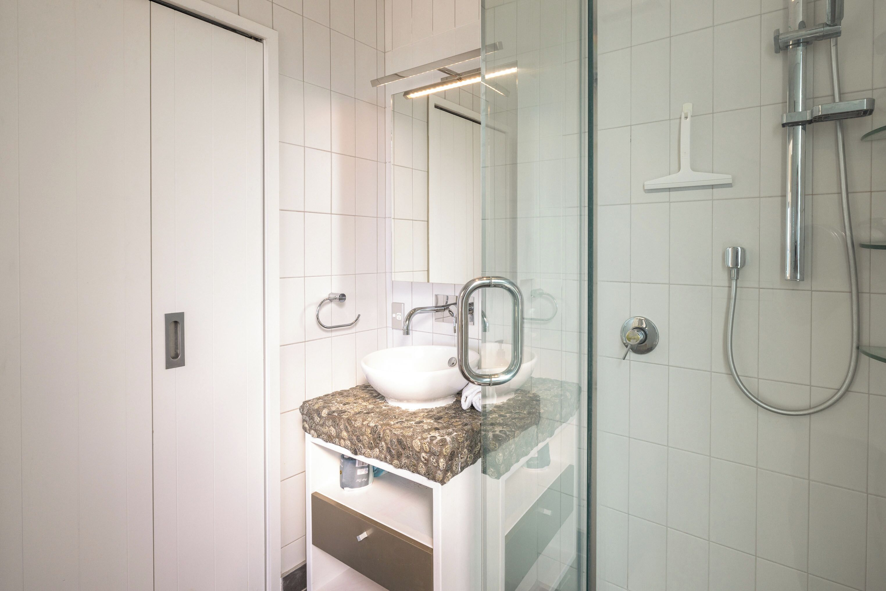 A modern bathroom with a glass shower enclosure, a white sink, and a marble countertop.
