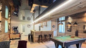 A spacious lounge with a pool table, bar area, and comfortable seating.