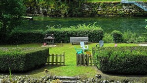 A riverside garden with a bench, chairs, and a small gazebo.