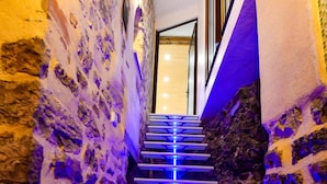 A staircase with blue lighting, stone walls, and a wooden door at the top.