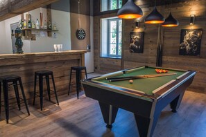 Una mesa de billar en una sala con paredes de madera, taburetes de bar y una zona de bar con botellas.