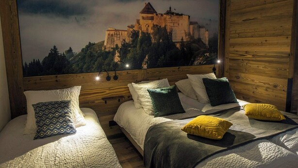 A room with two beds, wooden headboard, and a poster of Château de Joux.