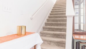 Eine Treppe mit Teppichstufen führt zu einer Zwischenebene, auf der ein weißer Tisch und ein goldfarbenes, zylindrisches Objekt stehen.