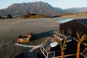 Un bâtiment moderne doté d’un balcon en verre donnant sur un vaste champ et des montagnes.