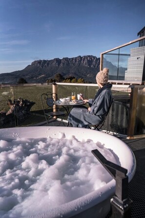 A person sitting at a table with a view of mountains, a glass-enclosed area, and a hot tub filled with bubbles.