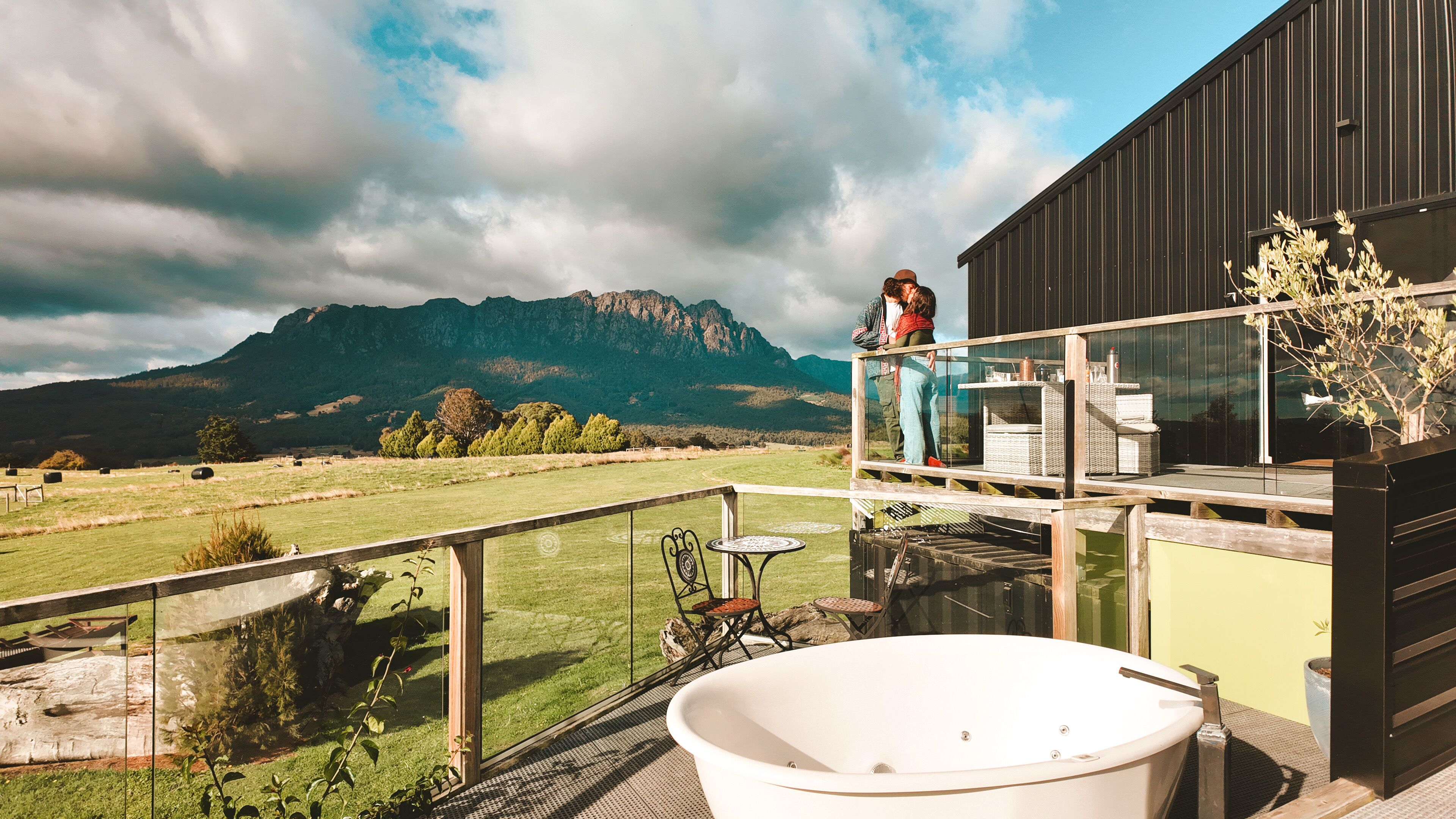 A balcony with a hot tub, a glass railing, and a view of mountains.