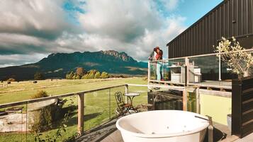 A balcony with a hot tub, a glass railing, and a view of mountains.