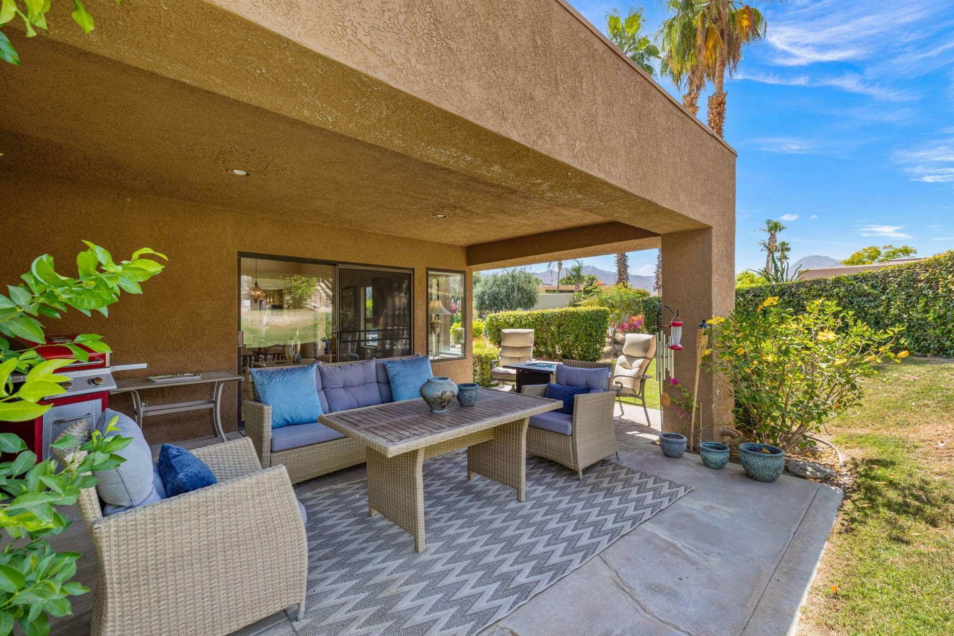 Un patio techado al aire libre con muebles de mimbre, una mesa y plantas en macetas.
