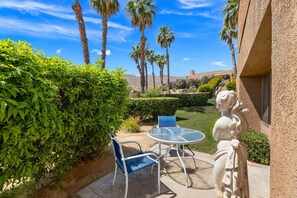 A patio with a table and chairs, surrounded by greenery and palm trees. - Elegant Retreat near El Paseo at Ironwood CC | Community Pool & Spa | BBQ | Haystack Green Belt (Palm Desert)