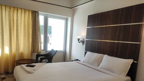 A hotel room with a large bed, a small table, a chair, and a window with curtains. - Nachiappa Palaniappa Grand Inn (Kodaikanal)