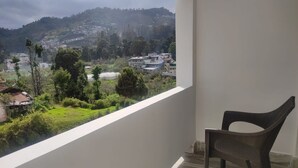 A balcony with a view of a hillside town, a chair, and a white wall. - Nachiappa Palaniappa Grand Inn (Kodaikanal)