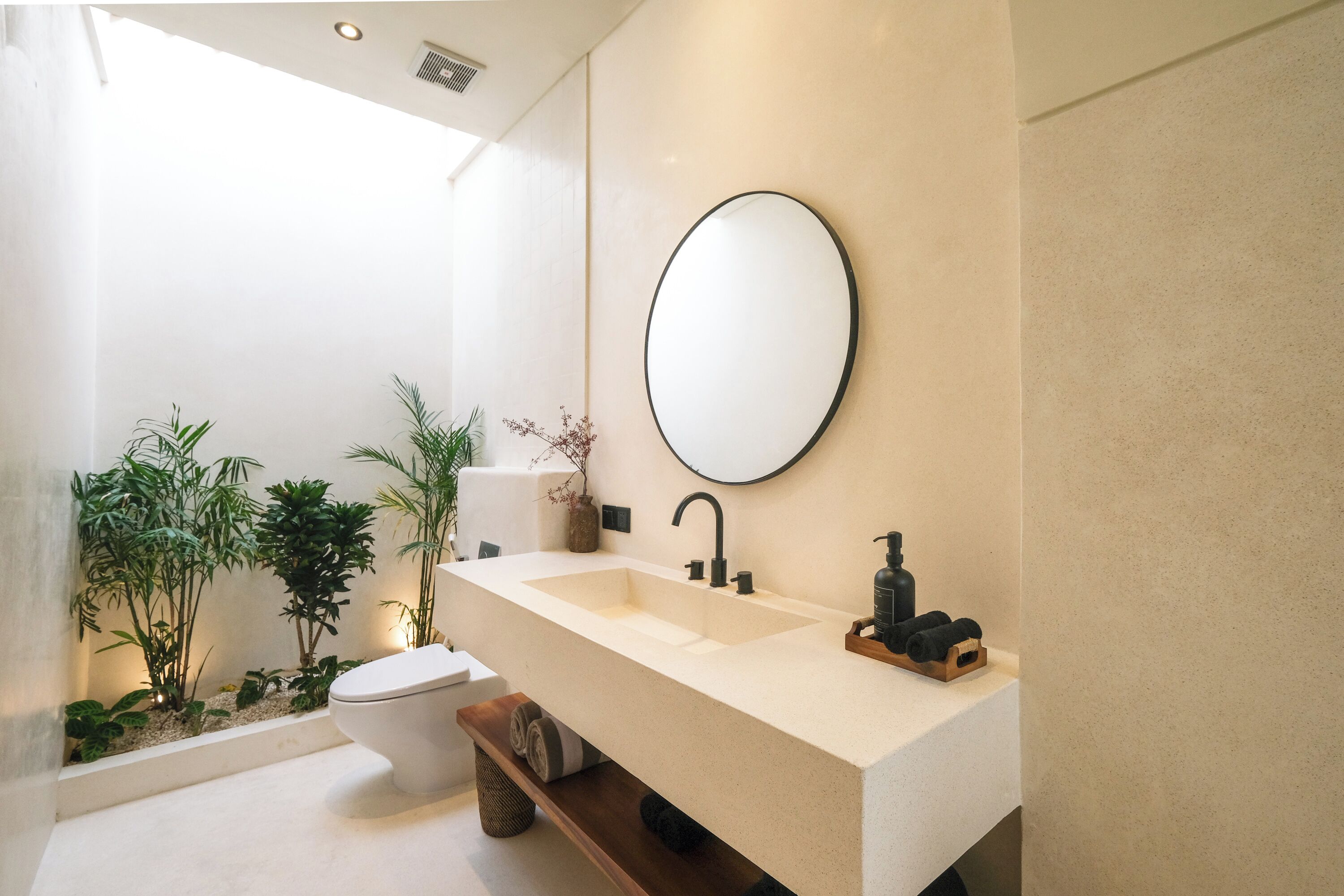 Un baño moderno con un lavamanos grande, un espejo redondo y plantas en macetas.
