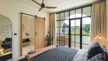 A modern bedroom with a large bed, a ceiling fan, a sliding door closet, a large window with curtains, and a view of the outside.