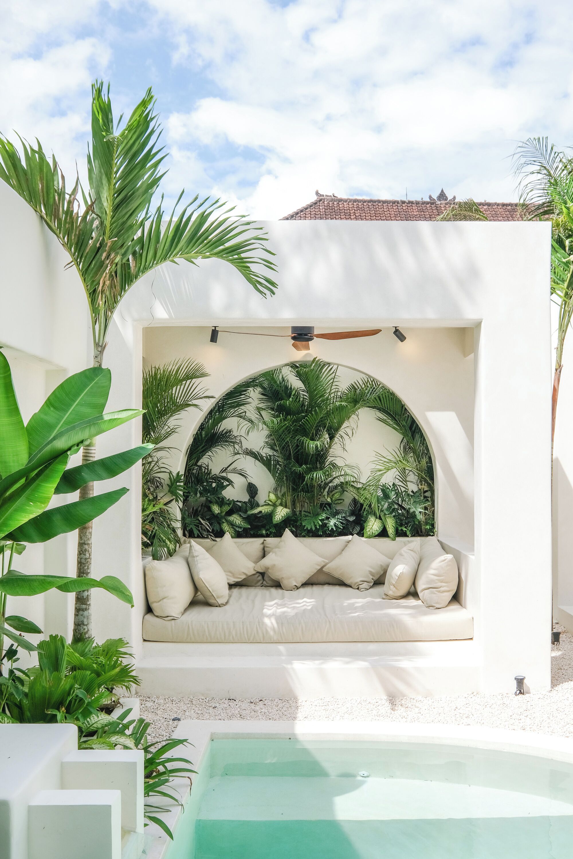 A cozy seating area with a white sofa and cushions, surrounded by lush tropical plants and a circular archway.