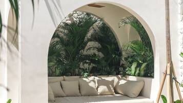 A poolside seating area with a cushioned bench, surrounded by tropical plants and a clear pool.